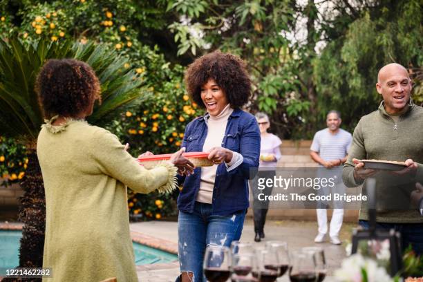smiling friends walking into backyard party with trays of food - gast stock-fotos und bilder