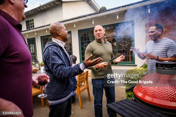mature men standing by barbecue grill talking - grill party stockfoto's en -beelden