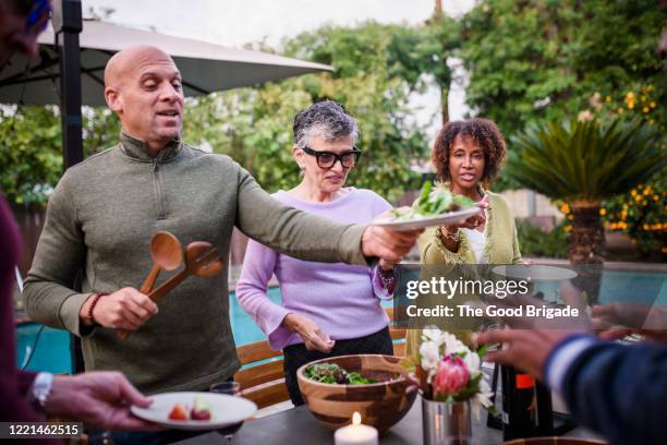 man serving friends salad at backyard dinner party - pool table stock-fotos und bilder