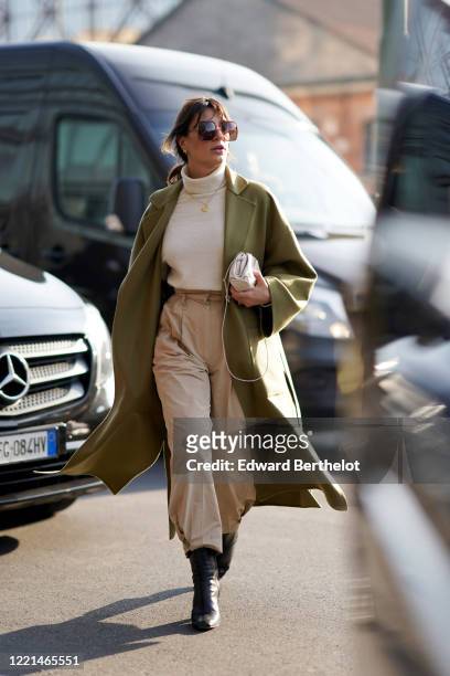 Carlotta Rubaltelli wears sunglasses, a white turtleneck pullover, a necklace, a green / khaki long coat, pale brown beige pants, pointy leather...
