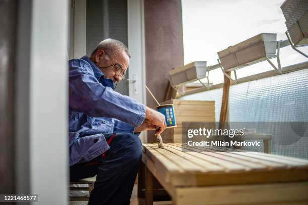 un uomo più anziano applica una mano di vernice a una superficie di legno - wooden surface finishes foto e immagini stock