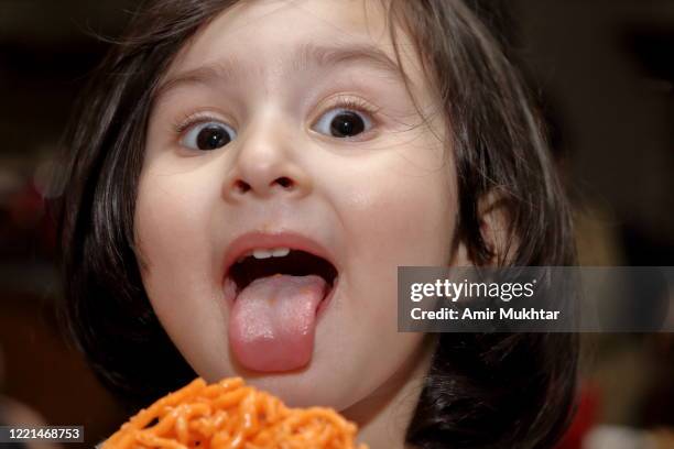 a closeup of a cute little girl with her toung out while eating candy (jalebi) and looking at the camera. - tongue stock pictures, royalty-free photos & images