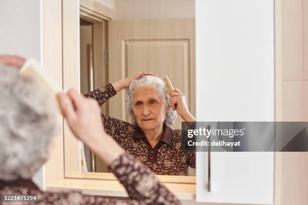 over the shoulder view of an elderly woman brushing her hair with a comb in hand in the bathroom - brushed back hair stock pictures, royalty-free photos & images