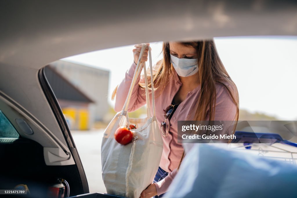 Woman with face mask loading car after shopping while covid-19.