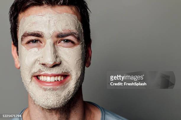 skin care: studio portrait of a happy handsome man with a clay facial mask on his face - man eye cream stock pictures, royalty-free photos & images