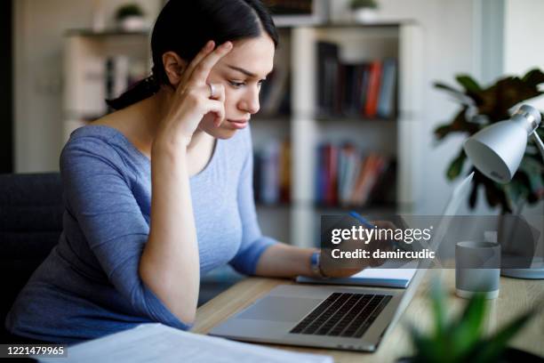 giovane donna preoccupata che lavora su laptop a casa - bill legislation foto e immagini stock