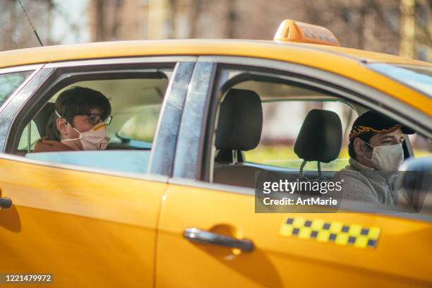 taxi driver and his passenger are wearing protective masks during air pollution or illness epidemic - yellow taxi stock pictures, royalty-free photos & images