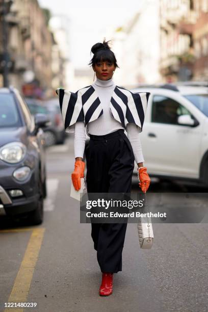 Guest wears a white turtleneck pullover, a black and white striped jacket with large shoulder pads, balck pants, a white quilted bag, red shiny...