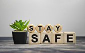 STAY SAFE - text on wooden cubes, green plant in black pot on a wooden background