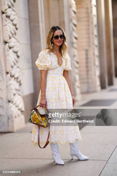 Guest wears earrings, sunglasses, a white and yellow dress with embroidery, a Loewe bag, white pointy leather boots, outside Vivetta, during Milan...