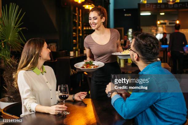 junge kellnerin serviert junges paar im restaurant - gast stock-fotos und bilder