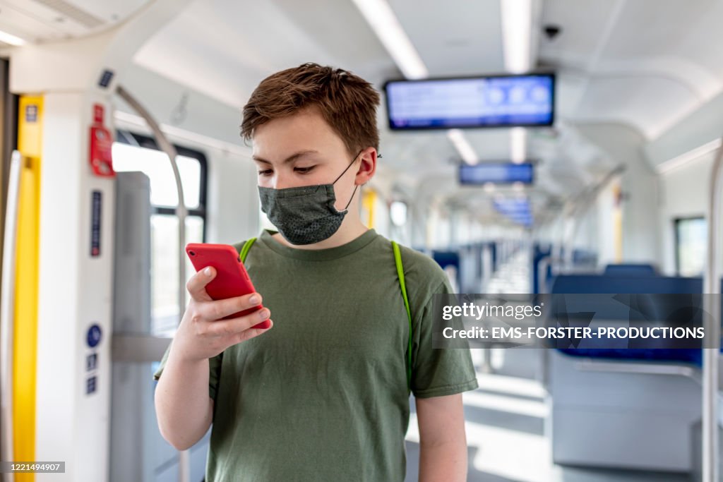 Schoolboy wearing protective, self made cotton mask and gaming on phone while travelling in train s-ban