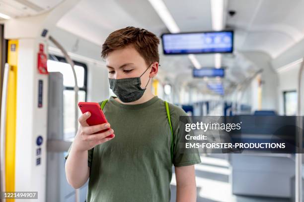 schoolboy wearing protective, self made cotton mask and gaming on phone while travelling in train s-ban - abstand halten infektionsvermeidung stock-fotos und bilder