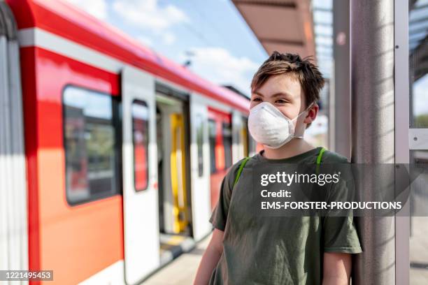 schoolboy is wearing a protective ffp-2 mask to prevent from corona virus while waiting at train station - surgical mask stock-fotos und bilder