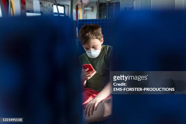 young boy wearing mask while he is tapping on his mobile phone - schüler smartphone stock-fotos und bilder