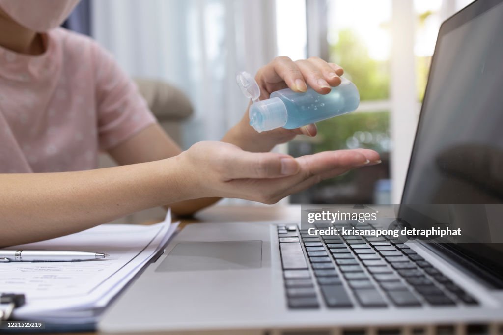 Business woman wearing face mask working in home with laptop and using hand alcohol gel or sanitizer bottle dispenser against coronavirus.Washing Hands, Illness Prevention, Hygiene, or Disinfection, where relevant.