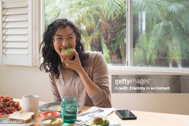 young woman eating avocado toast at home - abocado fotografías e imágenes de stock