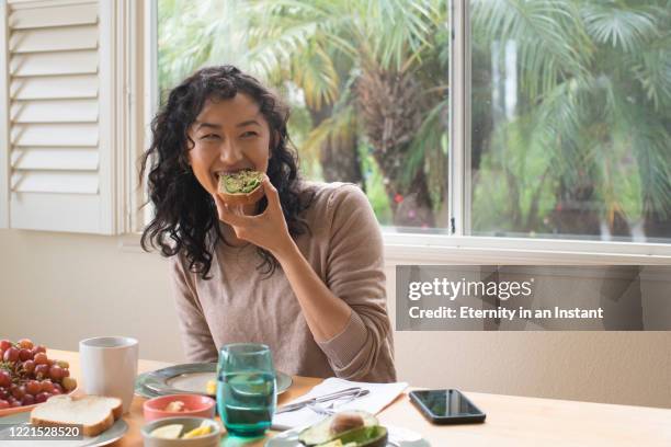 young woman eating avocado toast at home - avocados ストックフォトと画像