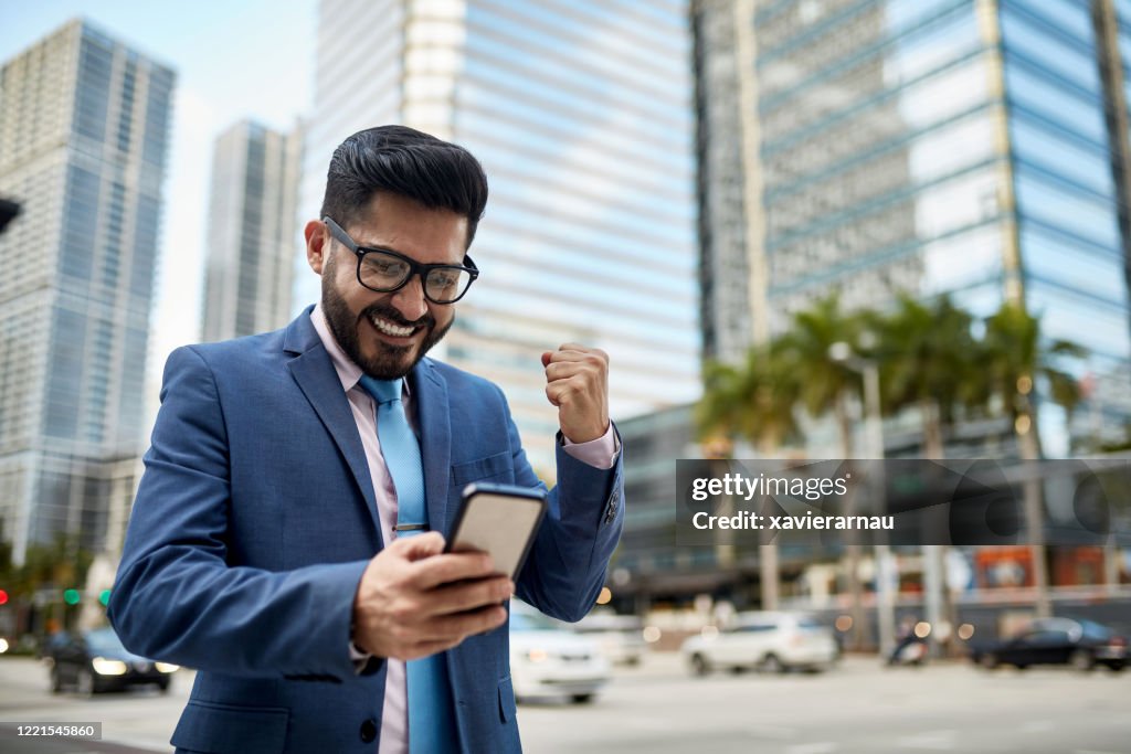 Sonriente Miami empresario leyendo buenas noticias en el teléfono inteligente
