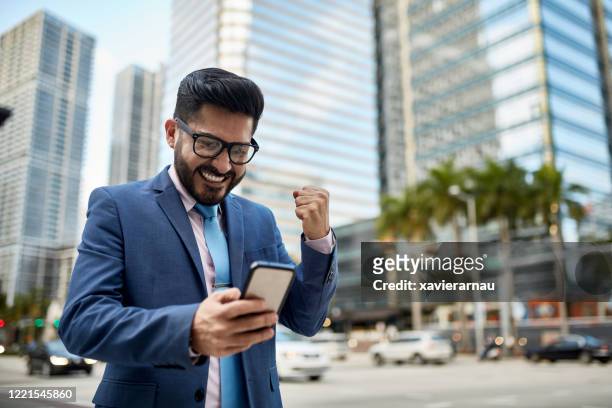 glimlachende zakenman van miami die goed nieuws op slimme telefoon leest - yes stockfoto's en -beelden