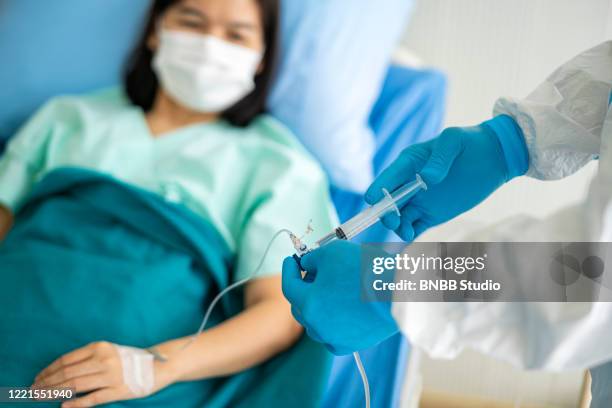 asian doctor in ppe medical suit with an injection vaccine and infusion drip for covid-19 or corona virus patient - infused - fotografias e filmes do acervo