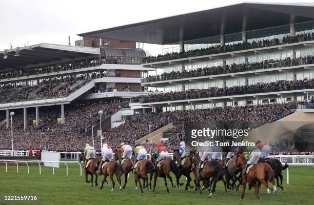 Runners in the first race pass by the packed main stands during day four of the Cheltenham National Hunt Racing Festival at Cheltenham Racecourse on...