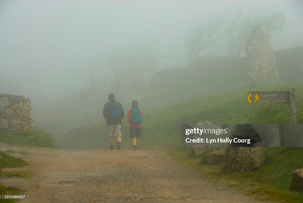 Back view of two hikers in mist walking along Wales Coast Path.