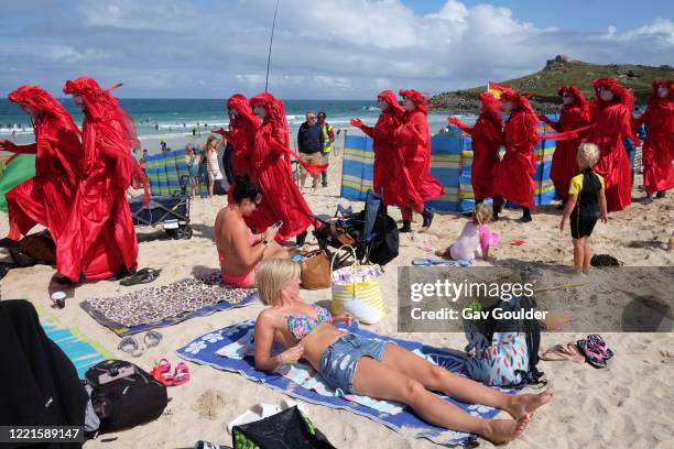 Spectacularly costumed Red Rebels lead a procession of Extinction Rebellion activists across Porthmeor Beach before entering the sea to stand in...