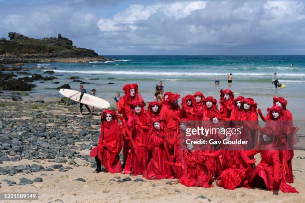 Spectacularly costumed Red Rebels lead a procession of Extinction Rebellion activists across Porthmeor Beach before entering the sea to stand in...