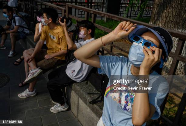 Chinese woman wears a protective mask to prevent COVID-19 and protective glasses as she watches the sun during the annular solar eclipse outside the...