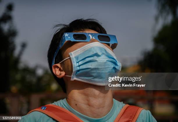 Chinese man wears a protective mask to prevent COVID-19 and protective glasses as he watches the sun during the annular solar eclipse outside the...