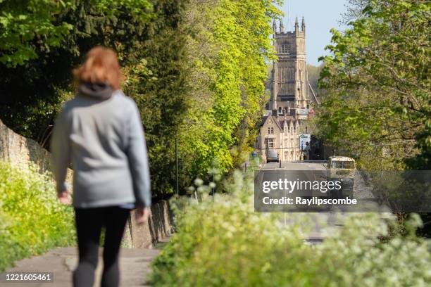 woman walking towards cirencester town centre parish church in the cotswolds, gloucestershire, peeking out in between trees and foliage and a bright spring day - cirencester stock pictures, royalty-free photos & images