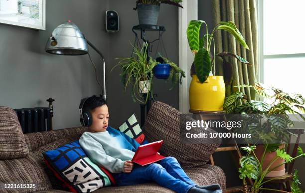 young chinese boy wearing headphones watching movie on tablet - digital native stock pictures, royalty-free photos & images