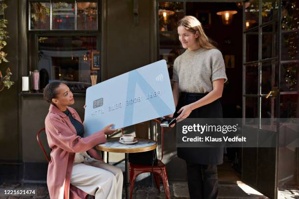 woman paying to barista through large credit card at sidewalk café - happiness scale stock pictures, royalty-free photos & images