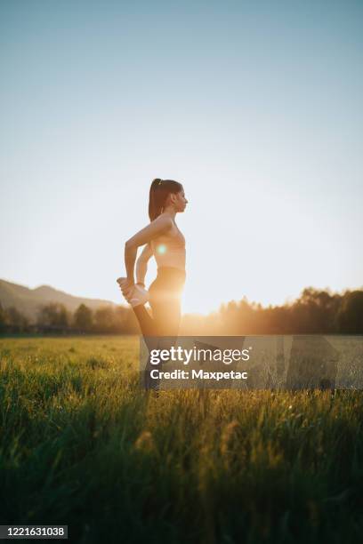 junge frau streckt sich im freien auf einem feld bei sonnenuntergang - woman stretching sunset stock-fotos und bilder