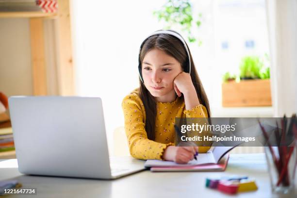 small schoolgirl with headphones and laptop sitting at the desk indoors at home, learning. - young girls homework stock-fotos und bilder