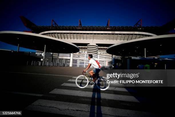 Man rides a bicycle past the Giuseppe-Meazza San Siro stadium prior to the Italian Serie A football match Inter vs Sampdoria, played on June 21, 2020...