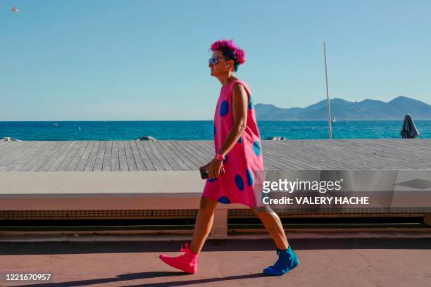 Woman wearing a colourful hairstyle, dress and shoes walks along the Croisette beach in the French riviera city of Cannes, southern France, on June...