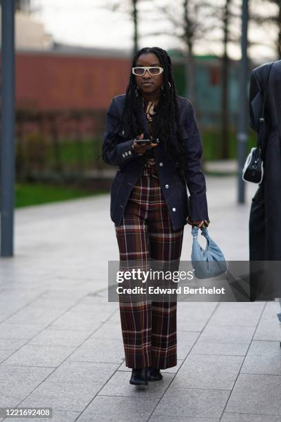 Guest wears sunglasses, a jacket, checked brown pants, a blue leather bag, during London Fashion Week February 2020 on February 17, 2020 in London,...