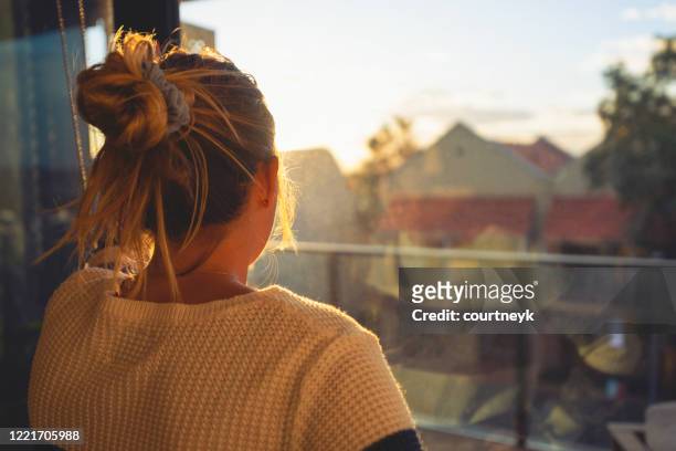 femme regardant par la fenêtre au coucher du soleil. - woman looking out of window photos et images de collection