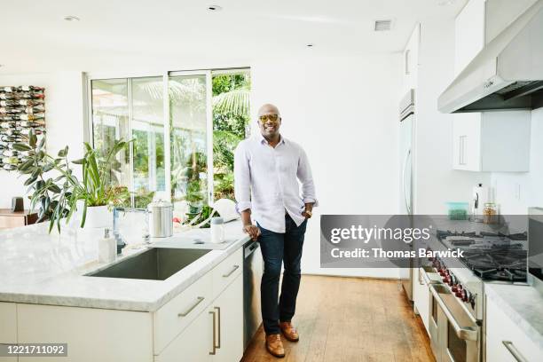 portrait of smiling man standing in kitchen after shopping for groceries - rolled up sleeves 個照片及圖片檔