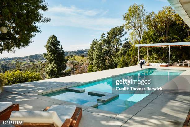 man seated by pool in backyard talking on smart phone - backyard pool fotografías e imágenes de stock