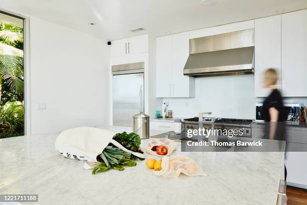 motion blur woman walking through kitchen with groceries in canvas bag on counter - return stock pictures, royalty-free photos & images