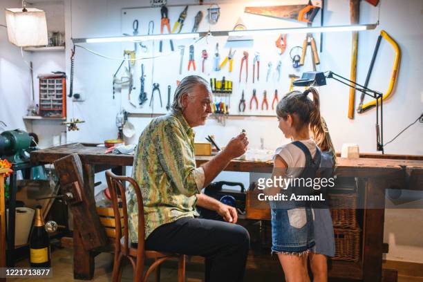 Grandfather Teaching Smiling Granddaughters in Home Workshop