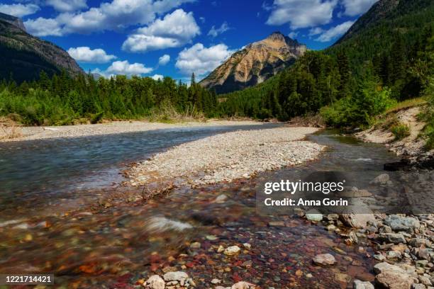 long exposure of mcdonald creek in west glacier national park, montana, on partly cloudy summer afternoon with tall mountains in distance - mcdonald creek stock-fotos und bilder