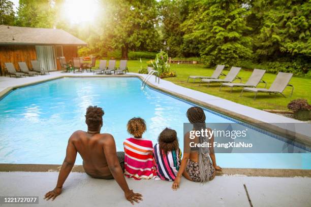 rear view of african-american family sitting on the edge of swimming pool at holiday villa backyard looking at sunset - end of summer stock pictures, royalty-free photos & images