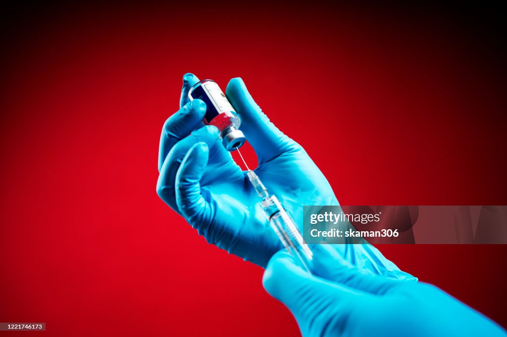 Doctor wearing Surgical gloves and preparing the coronavirus COVID-19 vaccine (2019-nCoV) first Coronavirus vaccine found in the world with red background isolated
