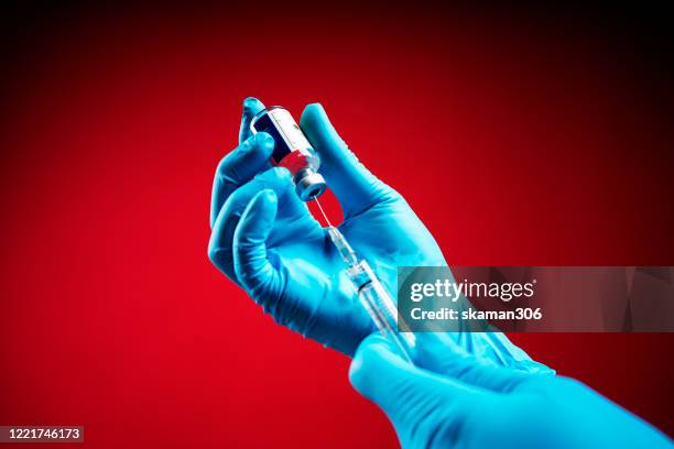 doctor wearing surgical gloves and preparing the coronavirus covid-19 vaccine (2019-ncov) first coronavirus vaccine found in the world with red background isolated - portrait studio shot stock pictures, royalty-free photos & images