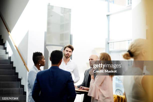 business people discussing while standing by table in office - kongressversammlung stock-fotos und bilder