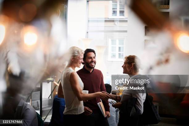 smiling businesswoman shaking hands with female coworker while standing by colleague in seminar at workplace - congress stock-fotos und bilder